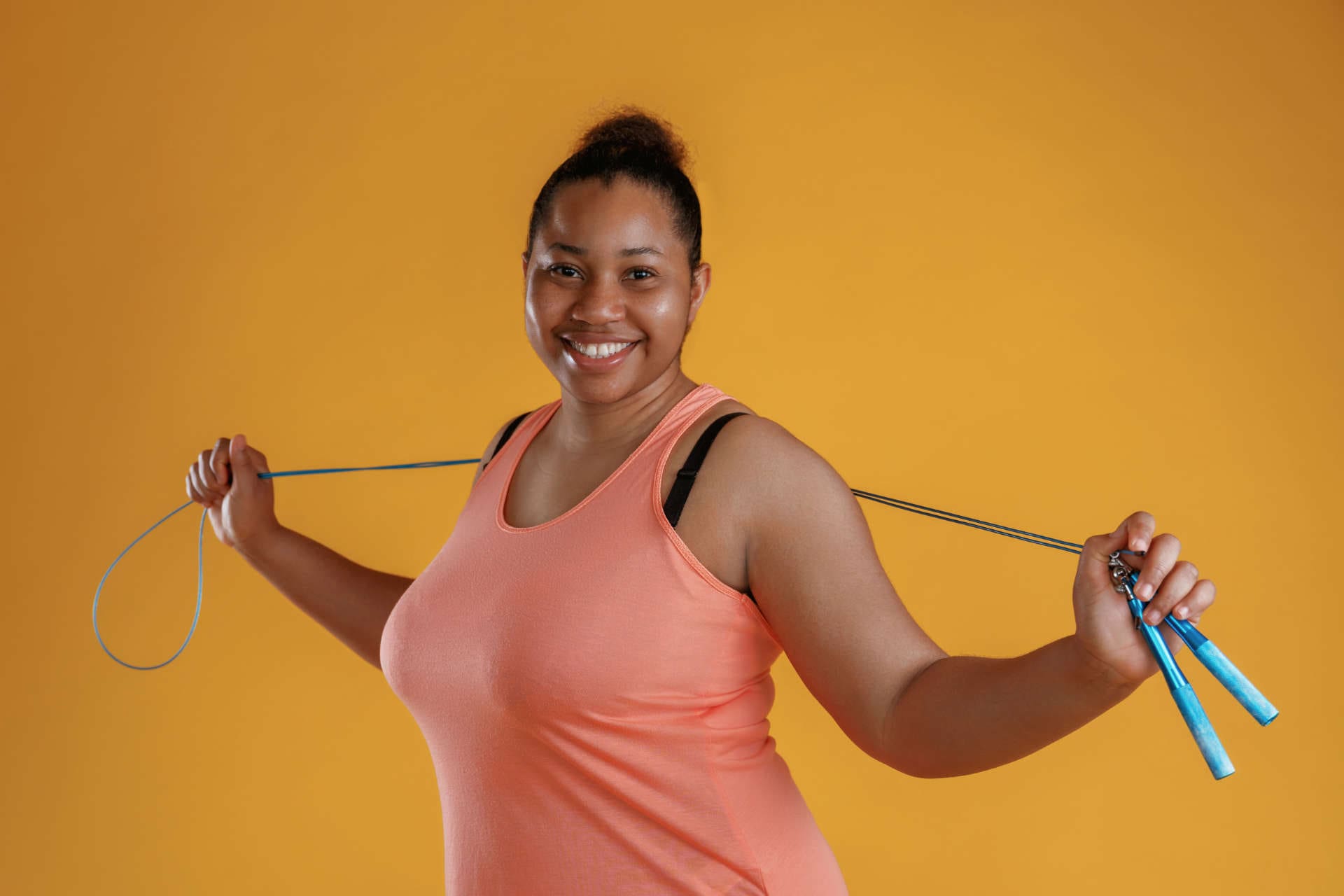 Jumping rope, standing. African American woman is in the studio against yellow background